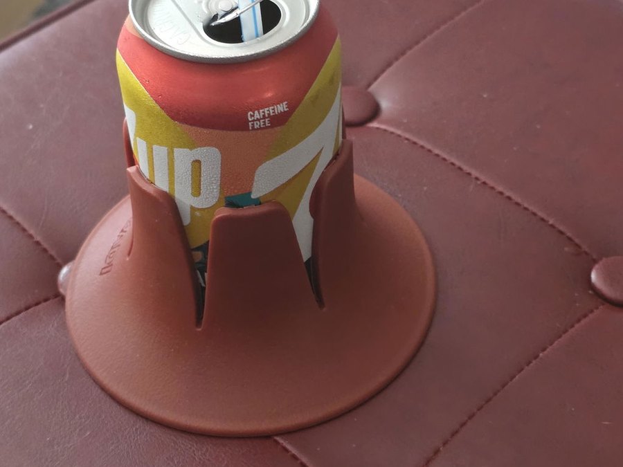 A burgundy drink base holding a red-and-yellow caffeine-free soda can with a blue straw, sitting on a tufted burgundy leather ottoman